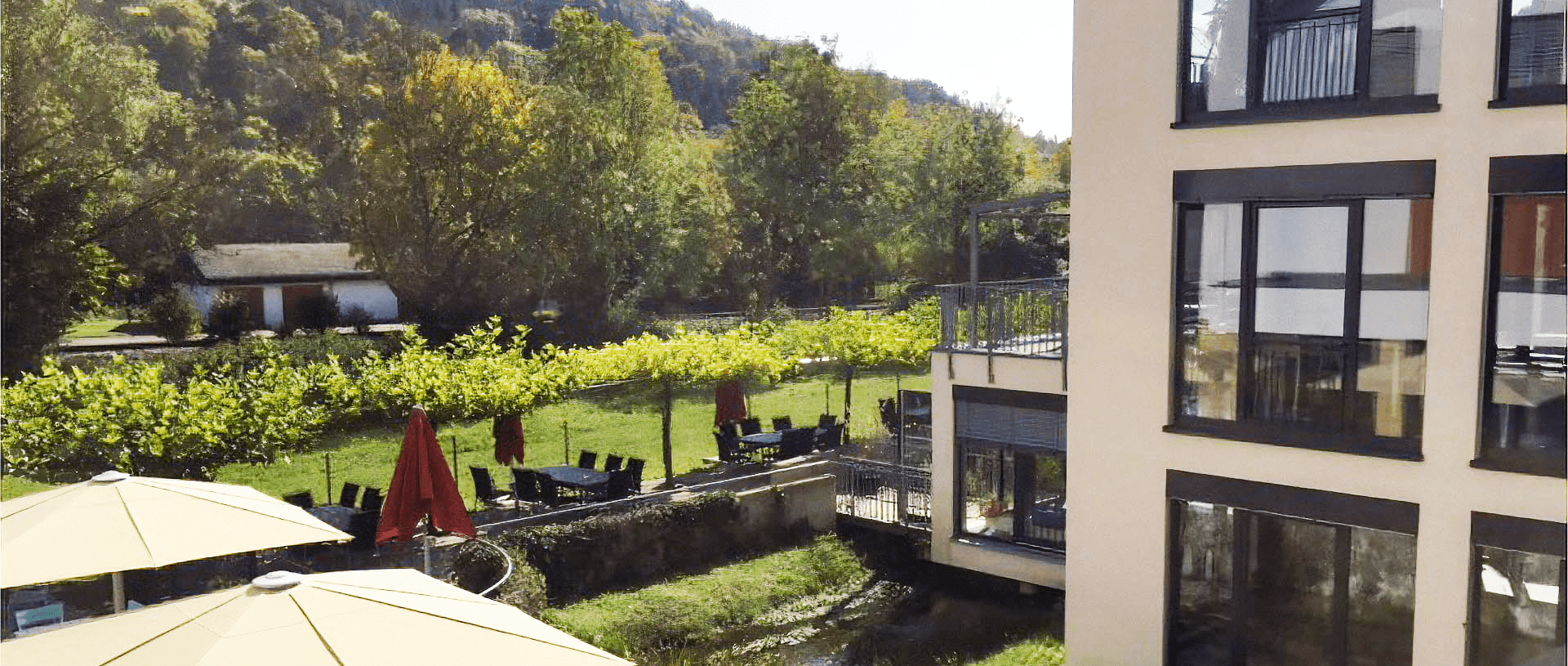 Sonnenterrasse mit Sonnenschirmen am Weilerbach, dahinter Garten und die bewaldeten Hänge des Schwarzwalds